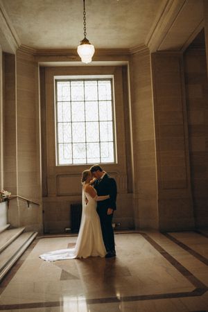 A couple shares their first dance in an elegant vintage ballroom with stained glass windows and warm lighting.