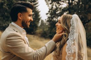 A tender moment between a couple in wedding attire sharing an intimate exchange in a wooded outdoor setting.