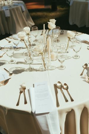 Elegant wedding reception table setting with white roses, crystal glasses and formal place settings.