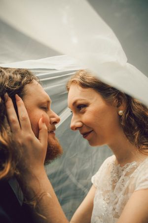 Bride and groom share an intimate moment under a flowing white veil on their wedding day.