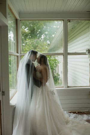 A romantic wedding moment silhouetted in a sunlit corner of an enclosed porch with flowing white veil and gown.