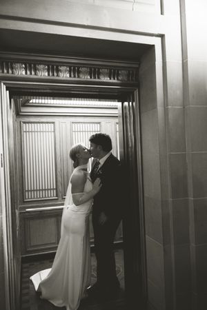 A romantic black and white sequence of a couple kissing in an elevator with elegant wood paneling.