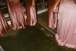 A group of people wearing pink bridesmaid dresses stand together on a dark carpet at a formal event.