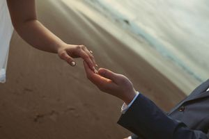 Groom placing a wedding ring on bride's finger during a romantic beach ceremony at sunset.