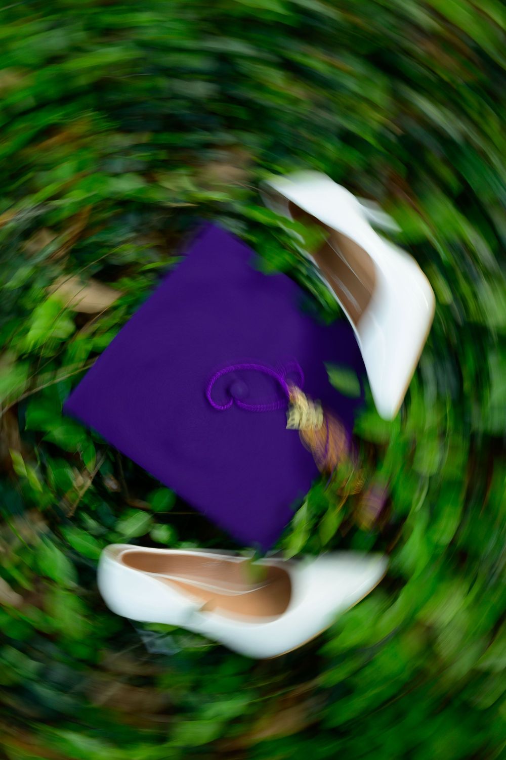 Purple graduation cap and white heels resting on green grass, captured with a swirling spin blur effect.