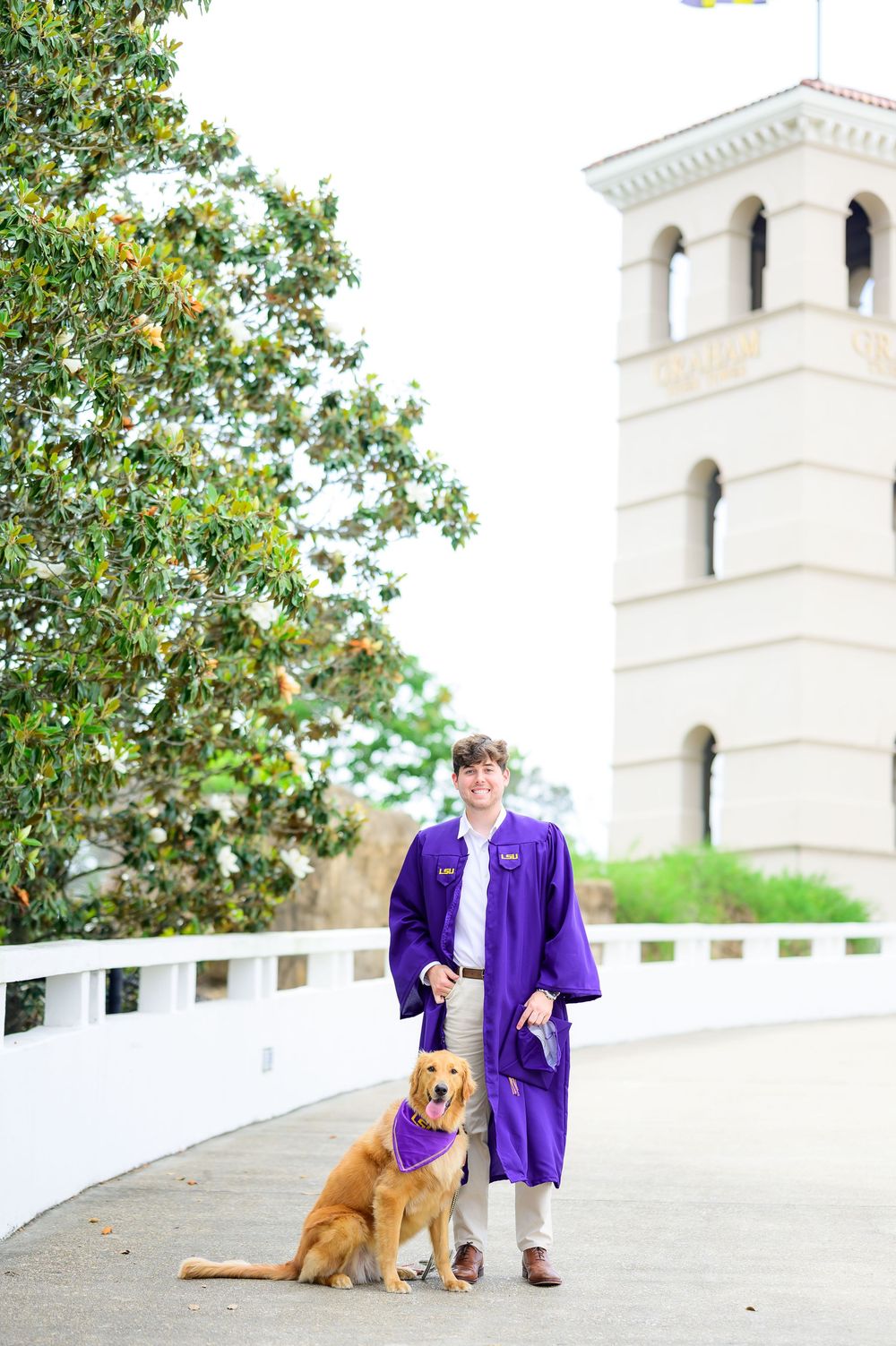 Graduate poses with golden retriever dog near white architectural columns.