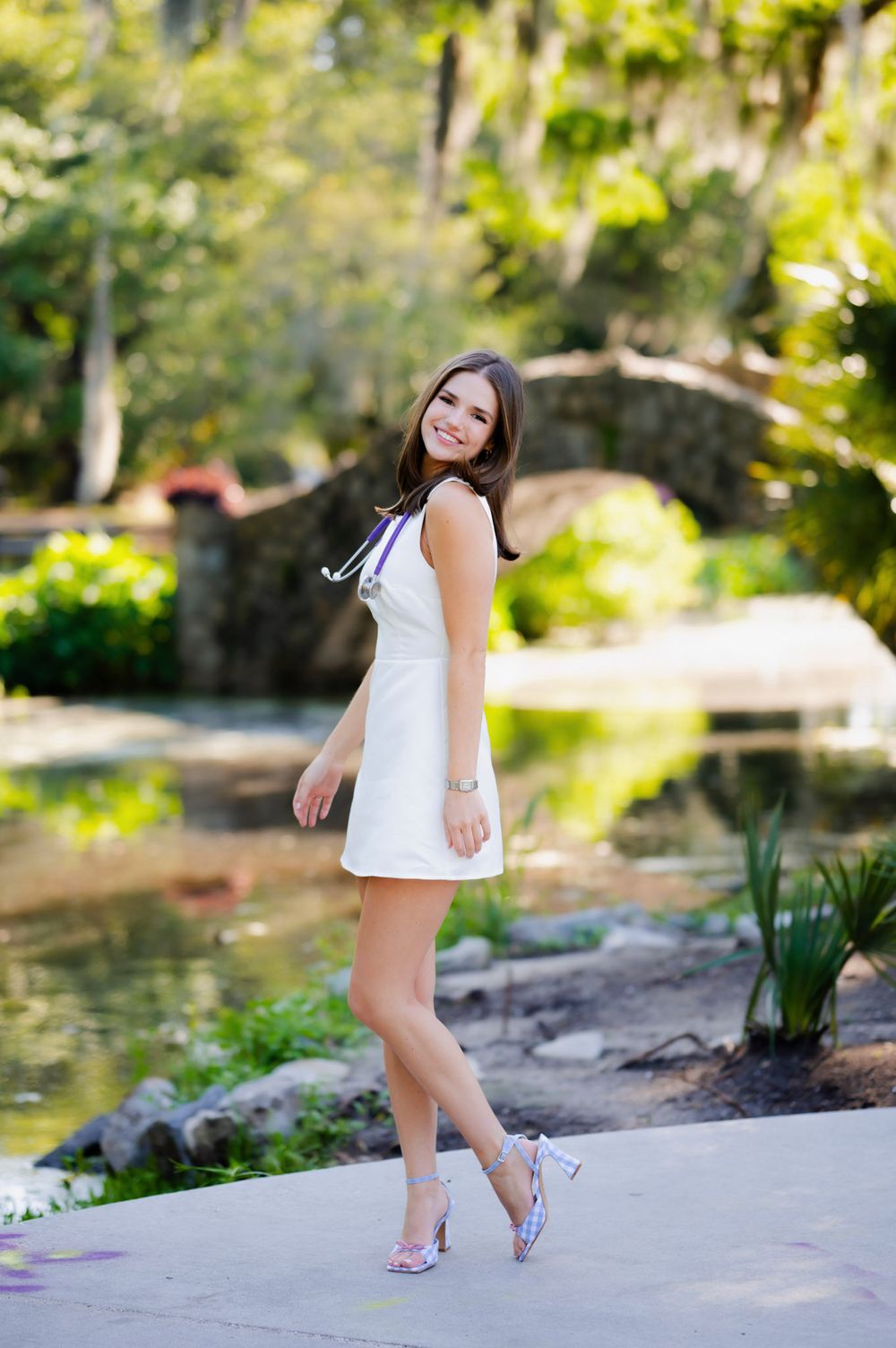 A summer photoshoot by a scenic pond wearing a white dress and heels.