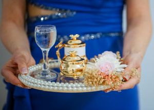 A blue-dressed server holds an ornate silver tray with wine glass and decorative items.