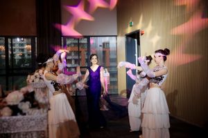 Dancers in white dresses performing at an evening event with pink lighting effects.