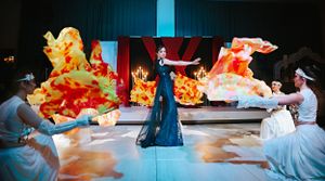 Artistic performance with dancers in flowing dresses against a dramatic red and orange backdrop.