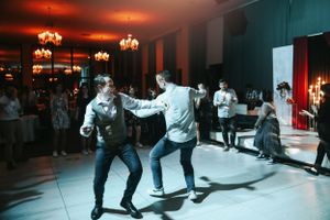People dancing energetically at a dimly lit indoor reception with elegant chandeliers.