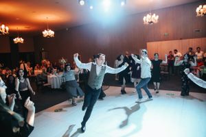 People dancing energetically on a dance floor under chandeliers at a wedding reception.