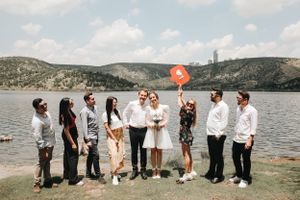 Wedding party poses with a heart balloon by a lake with mountains in the background.
