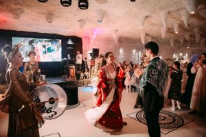 Couple dances together at a wedding reception in a cave-like venue with atmospheric lighting and guests watching.