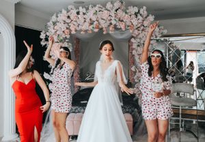 Wedding party celebrates under a pink floral arch during a festive moment.