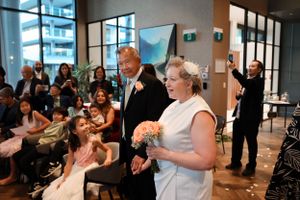 Wedding guests share a joyful moment during a reception in a modern venue with floor-to-ceiling windows.