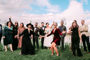 Wedding party poses energetically on grass during outdoor celebration.