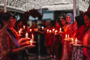 Group holds lit candles during an evening ceremony creating a warm red glow.