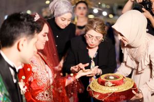 Wedding guests gather around a traditional ceremonial display with ornate decorations in red and gold.