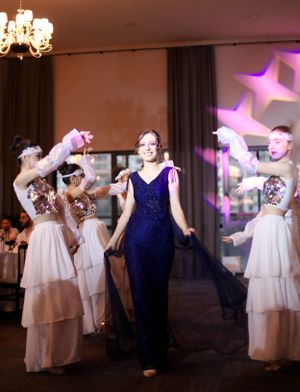 Elegant dance performance with person in blue gown surrounded by dancers in flowing white dresses.