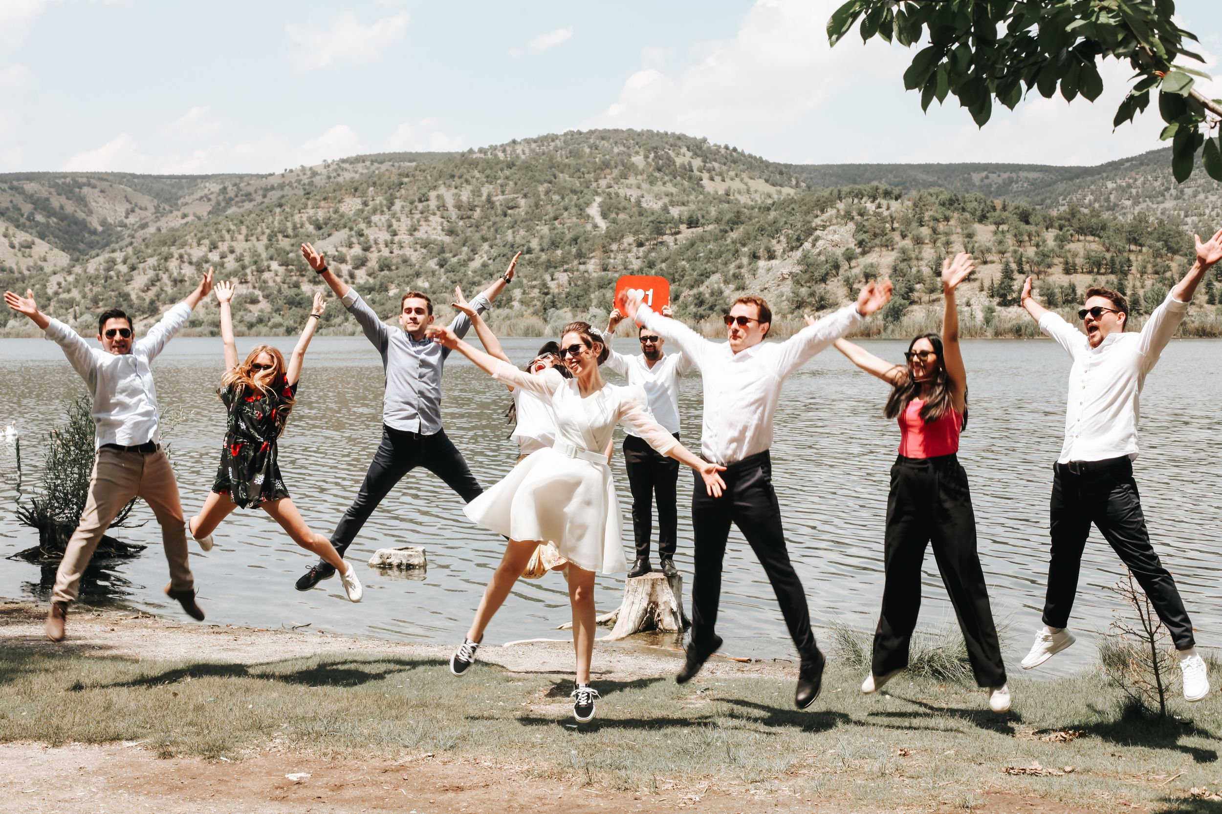 Wedding party leaps in the air against a backdrop of mountains and lake.