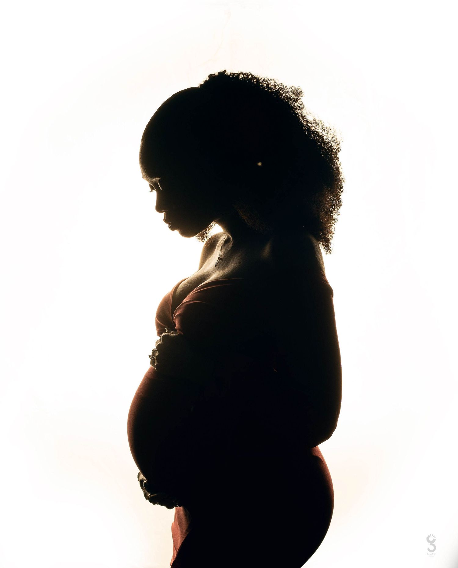 A silhouetted side profile of a pregnant woman with curly hair stands against a bright white background.