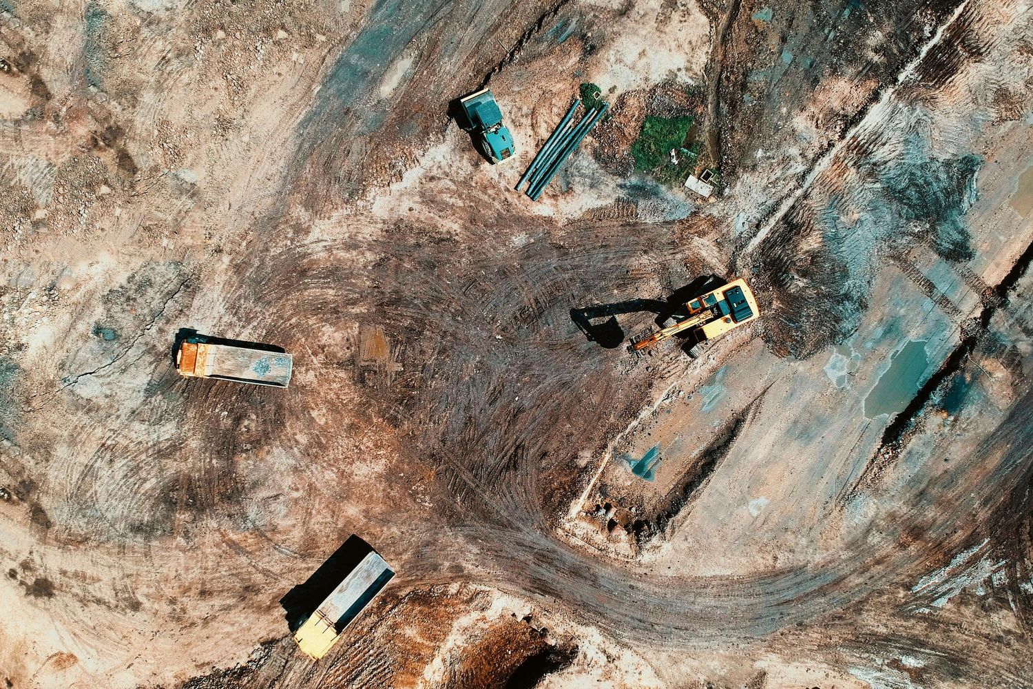 Aerial view of construction vehicles working on a curved dirt road through rocky terrain.