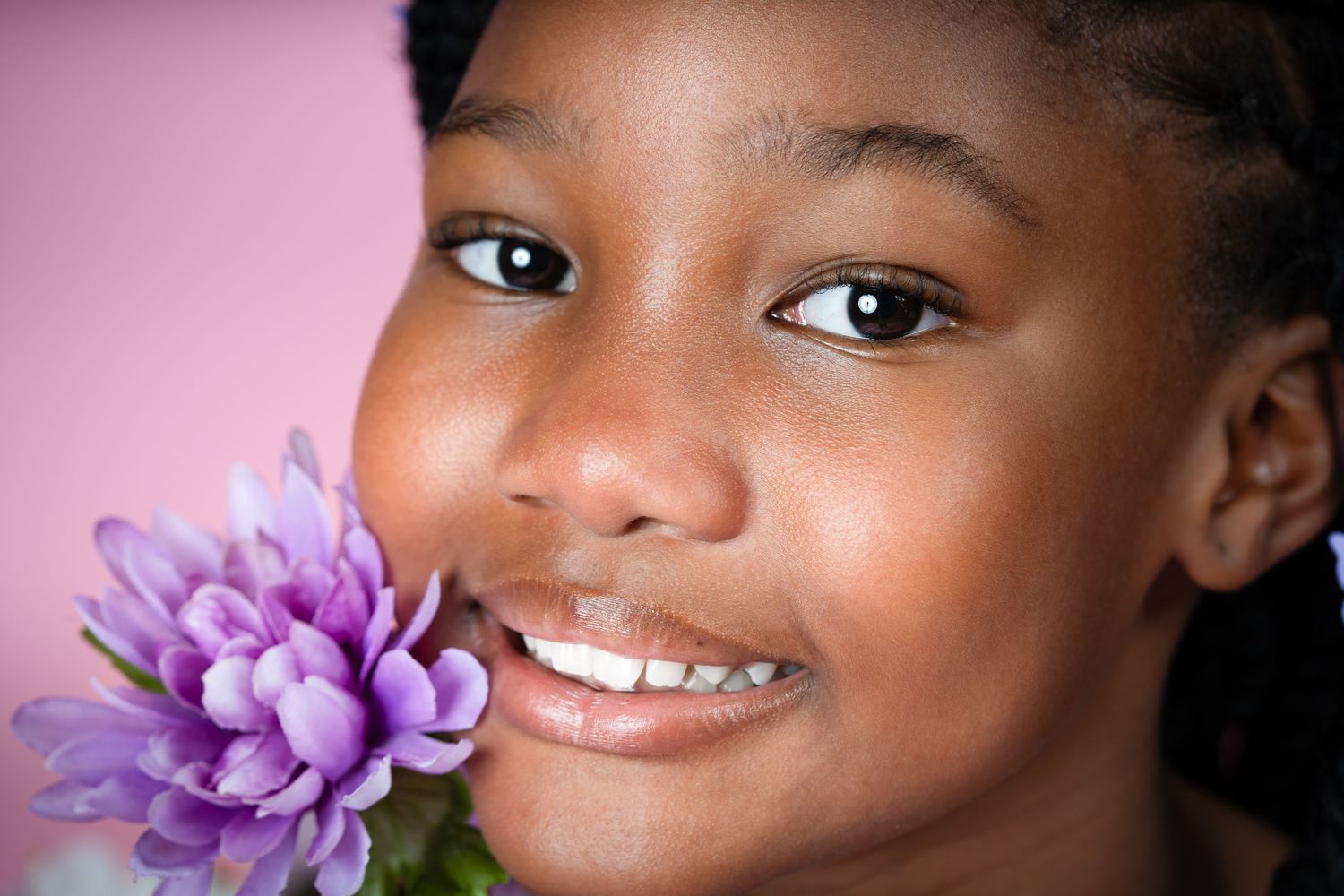 Close-up portrait with purple floral decorations against pink background.