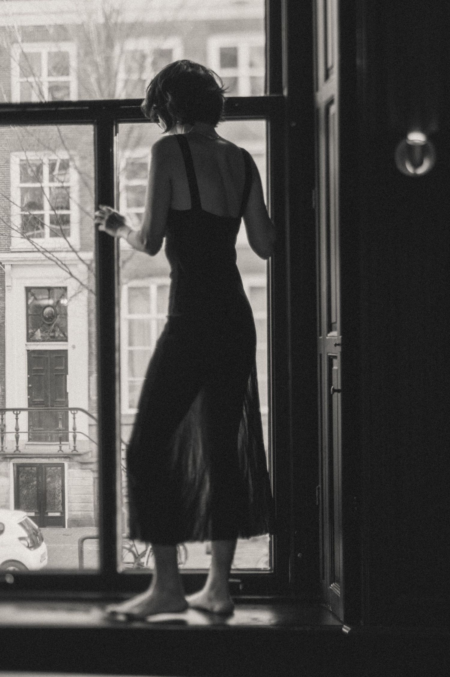Lifestyle candid photo in a cinematic style – a woman sitting on a windowsill, gazing outside. Intimate boudoir session.
