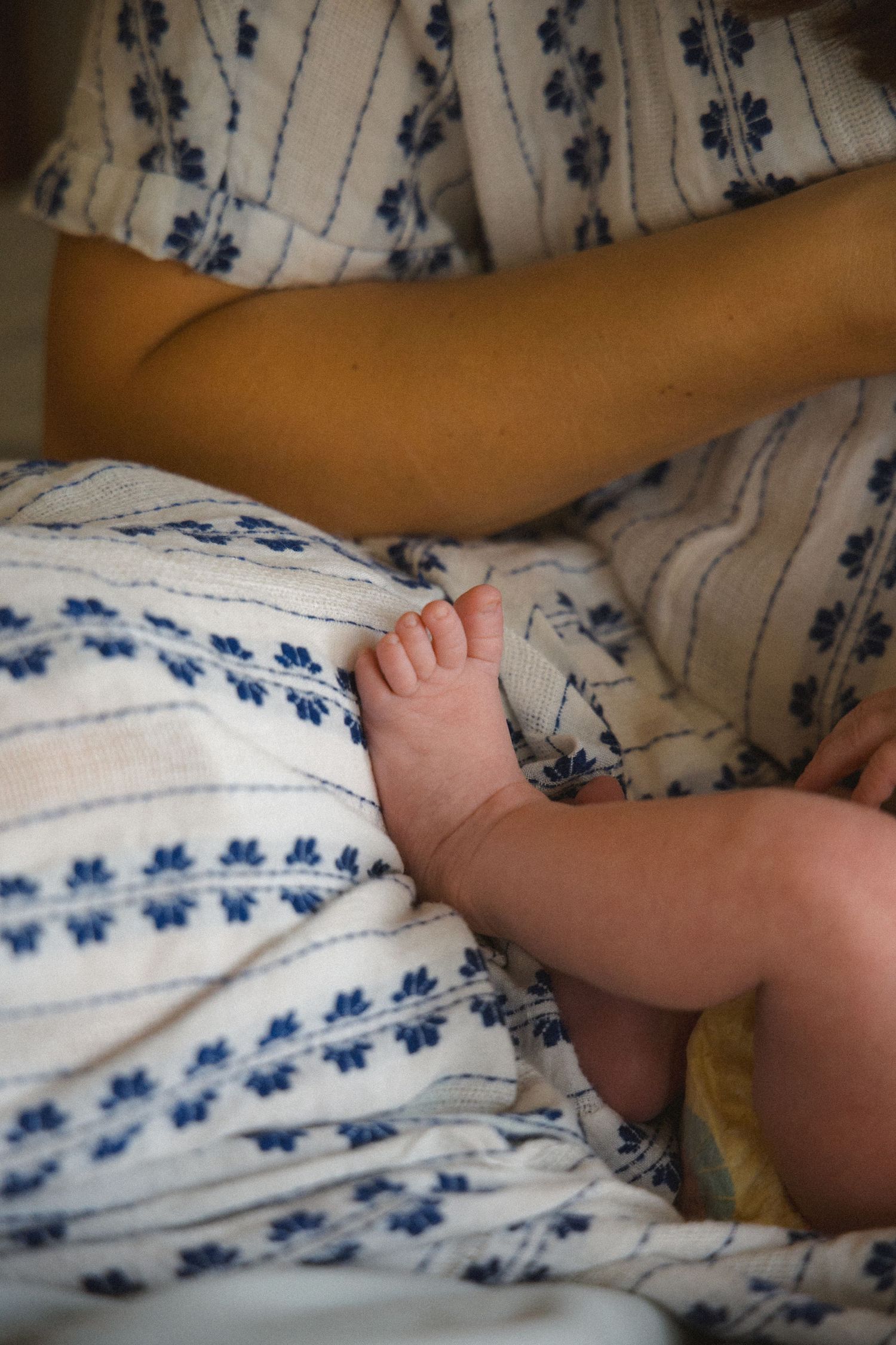 newborn tiny feet touching moms leg while nursing detail shot