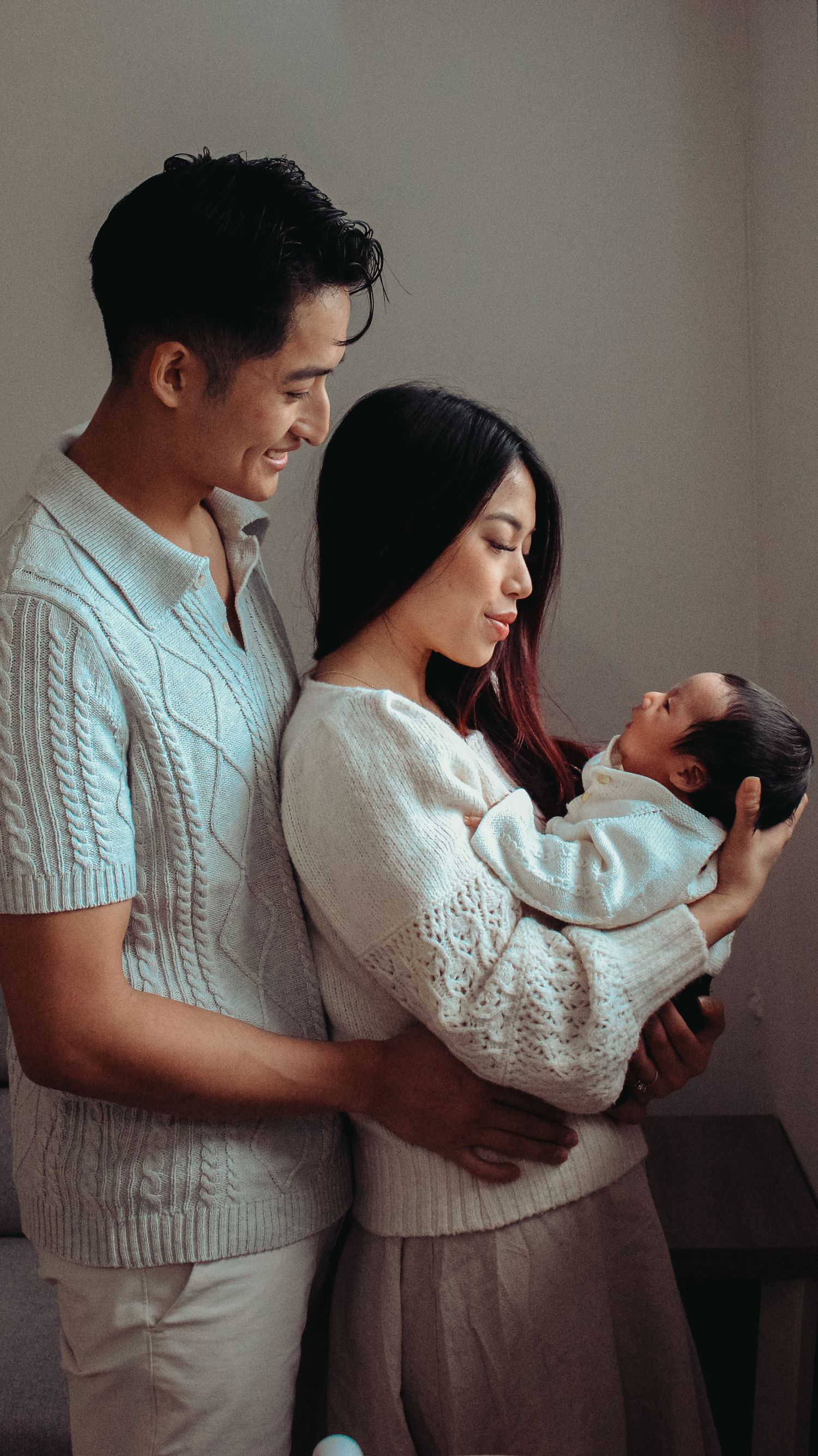 newborn being held by mom with dad standing behind her and looking at parents