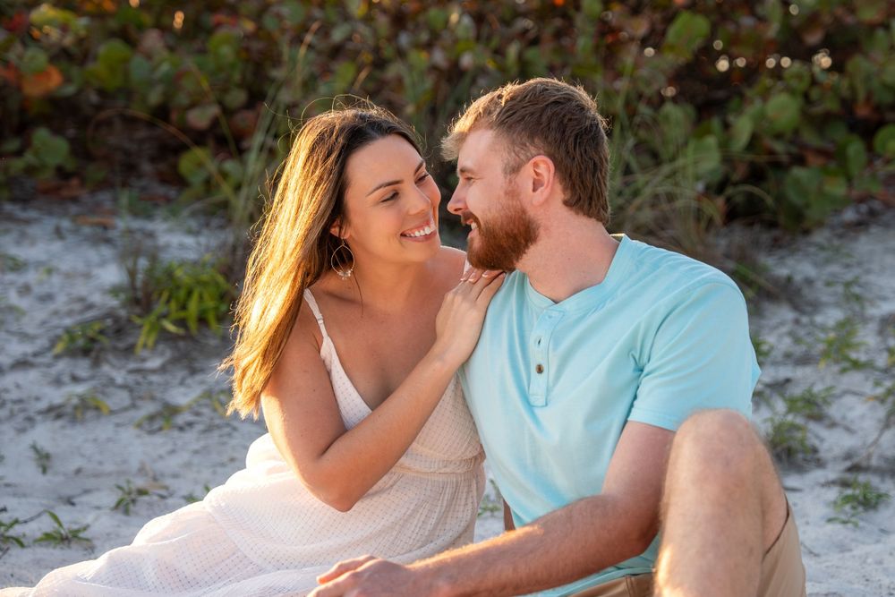 Happy couple sharing a tender moment on sandy beach dunes surrounded by lush green foliage at golden hour.