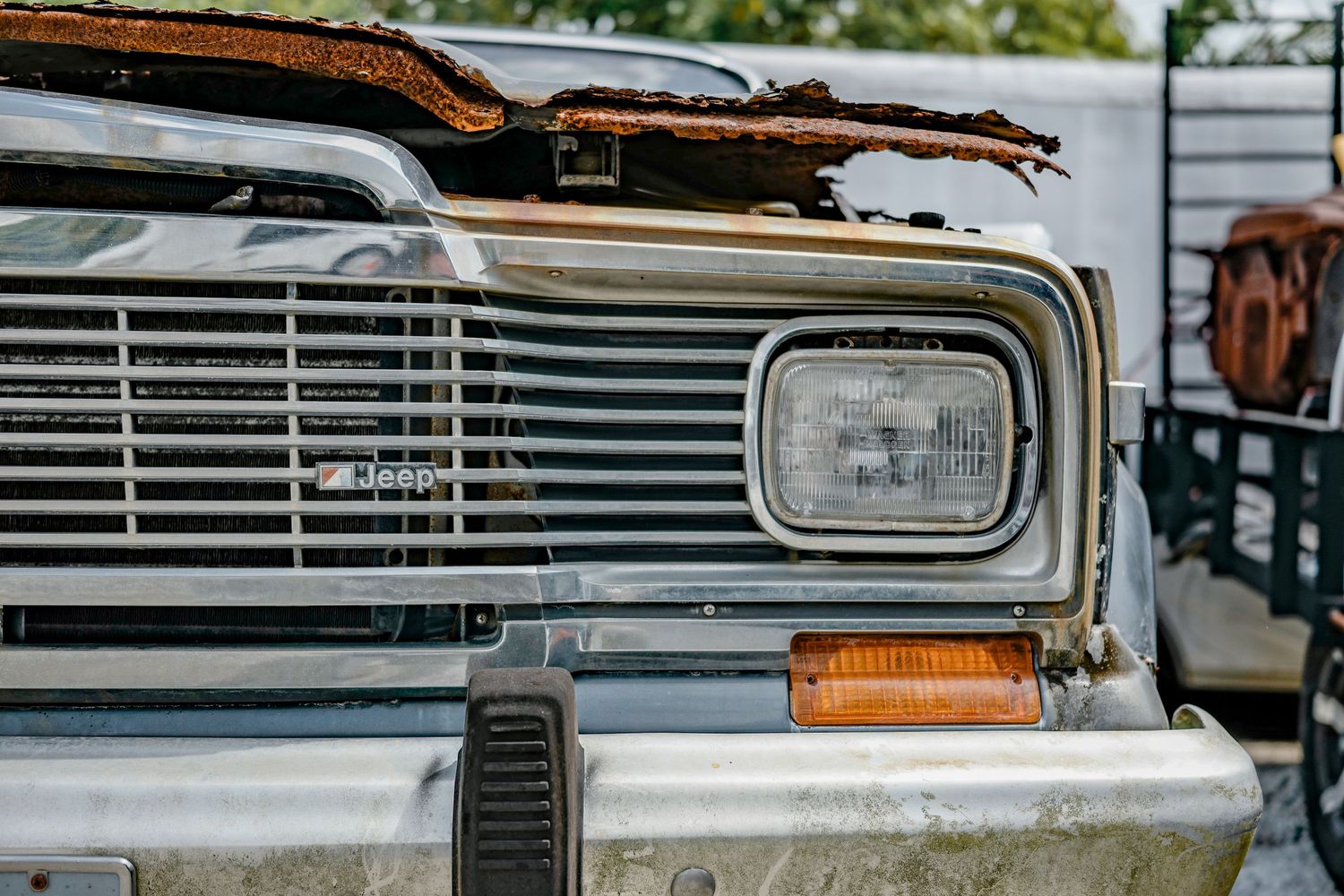 Close up of vintage car front end showing rusty chrome grille, headlight and amber turn signal.