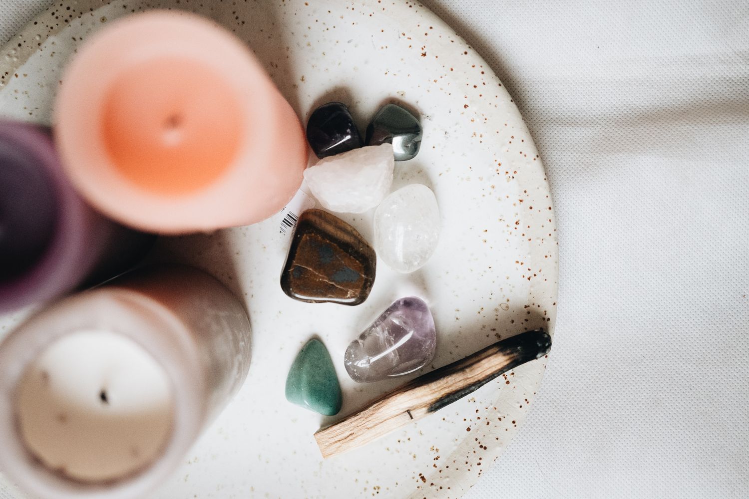 A collection of healing crystals and candles arranged on a white ceramic plate with sprinkled glitter.