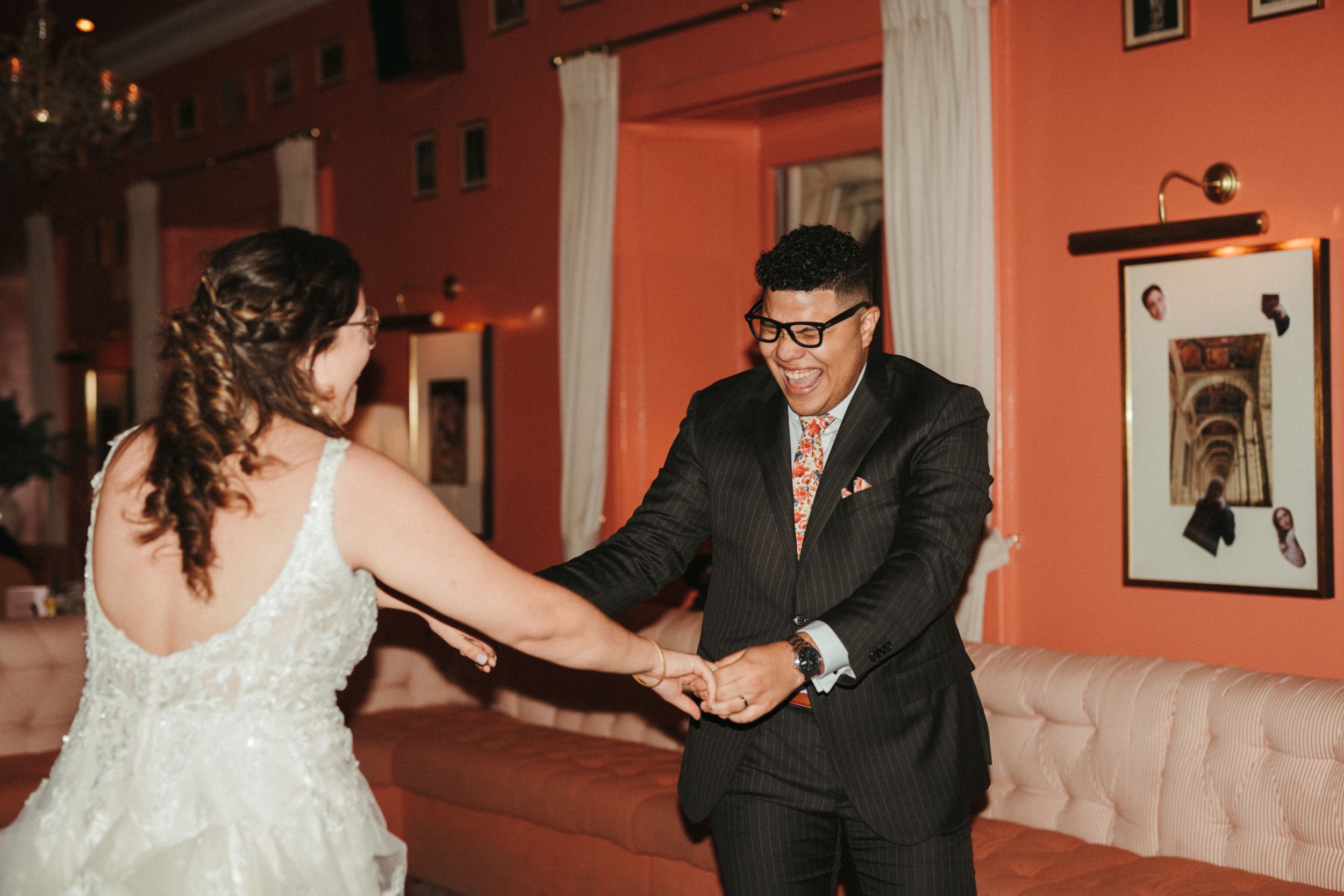 Couple dances joyfully together at a wedding reception in a room with coral-colored walls.