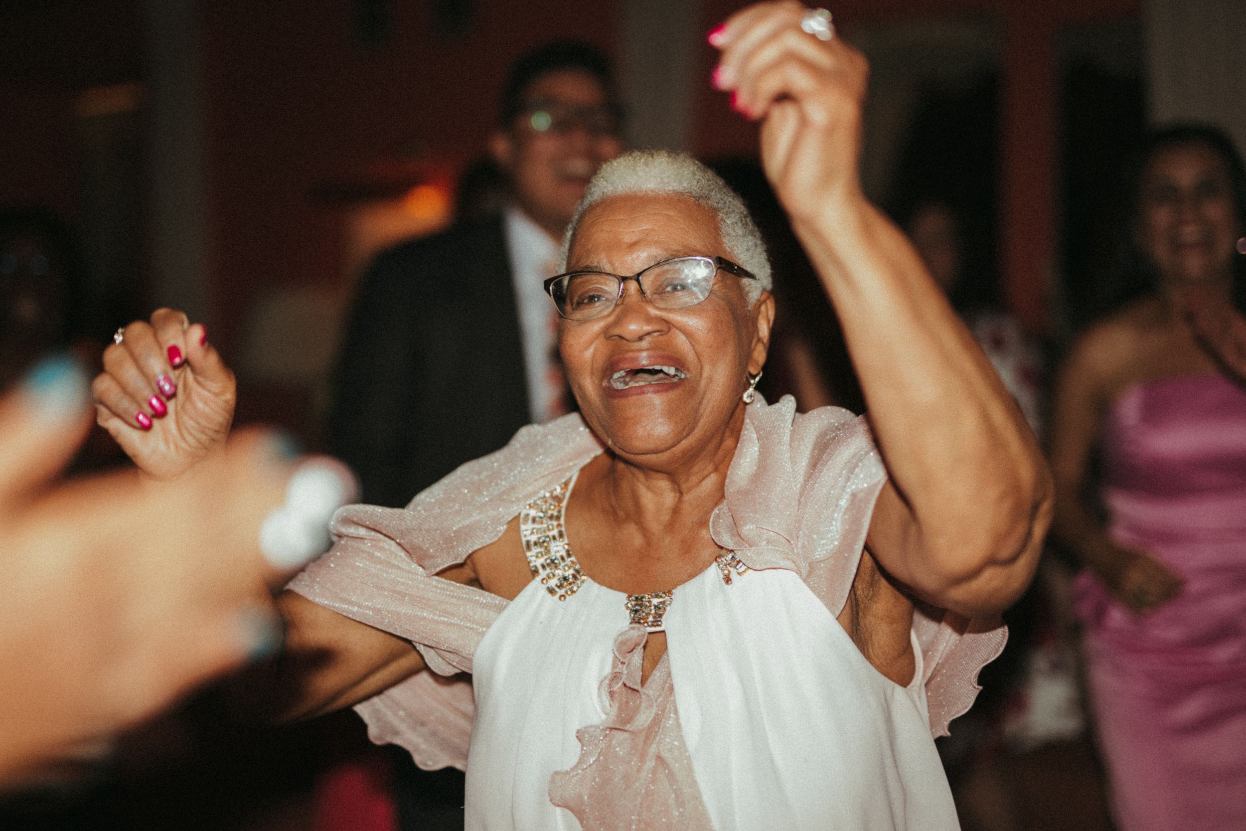 Enthusiastic dancer in glasses and white outfit joyfully moving on the dance floor at a celebration.