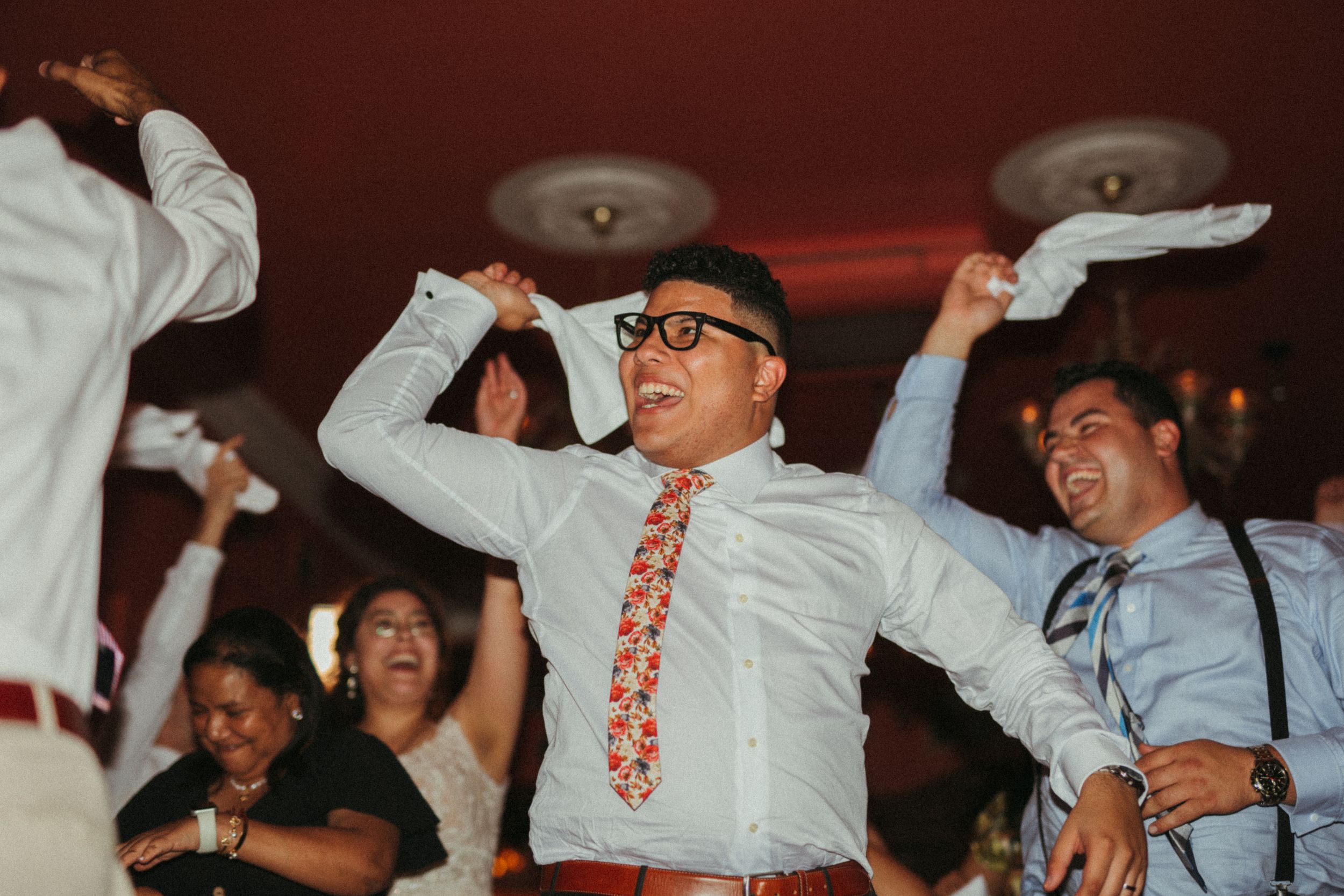 Enthusiastic dancers raise their arms while celebrating on the dance floor at a wedding reception.