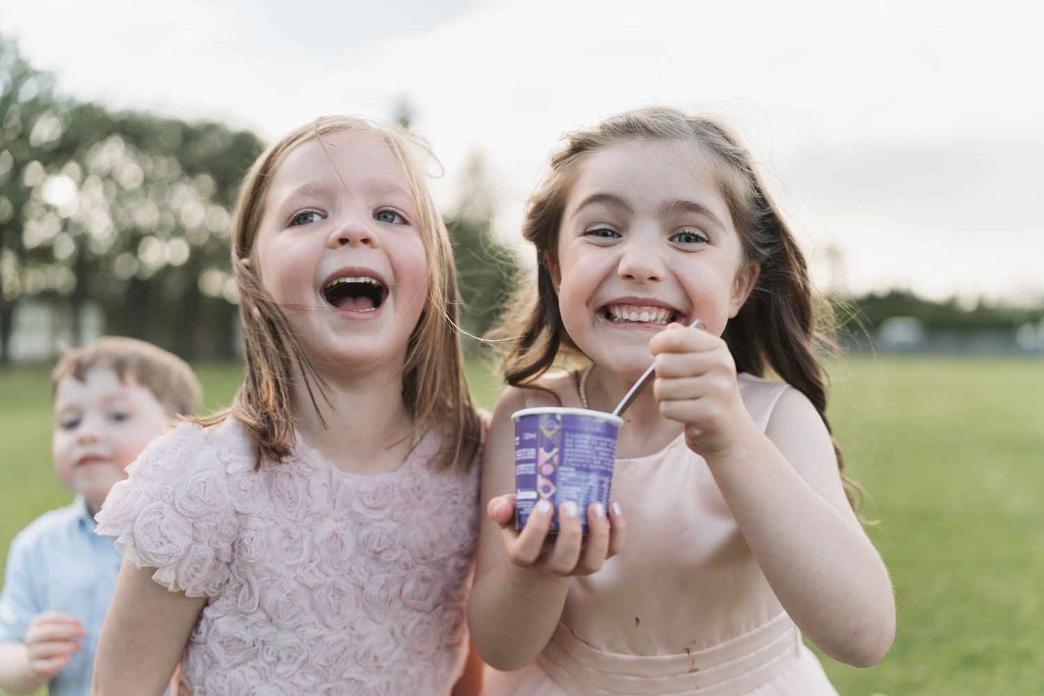 Children laughing and playing outdoors while holding a small purple jar in a grassy field on a sunny day.