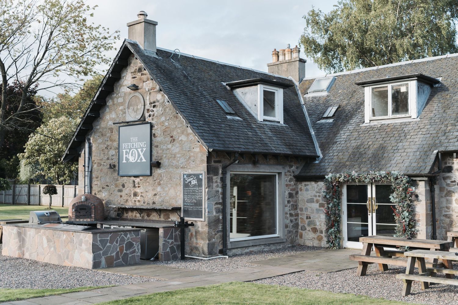 Rustic stone cottage with slate roof, dormer windows and wooden picnic bench in the garden exhibits traditional Scottish architecture.