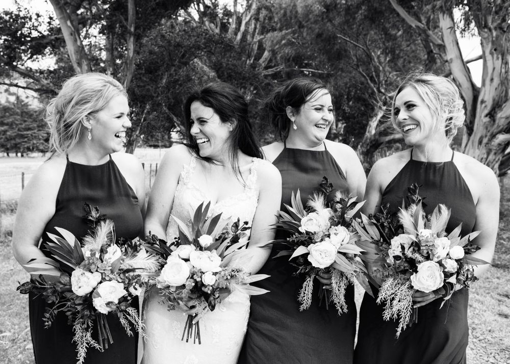 A joyful black and white wedding photo of bridesmaids in elegant dresses holding beautiful floral bouquets.