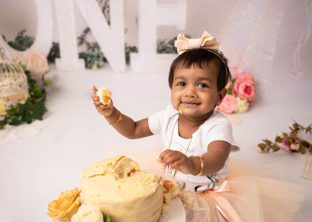 A toddler in a tulle dress celebrates with a smashed yellow birthday cake during a cake smash photo session.