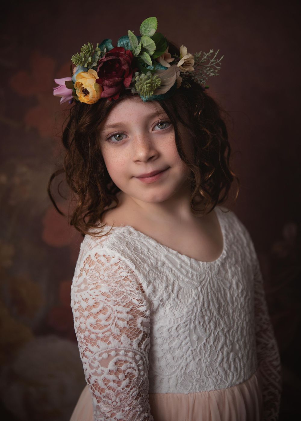 A soft portrait in neutral tones featuring delicate lace and a flower crown with burgundy blooms and greenery.