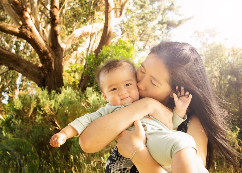 Parent and child share a tender moment embracing outdoors in golden sunlight with trees in the background.