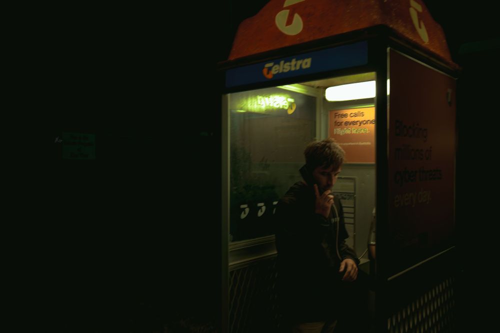Illuminated Telstra phone booth exterior with signage visible at night.
