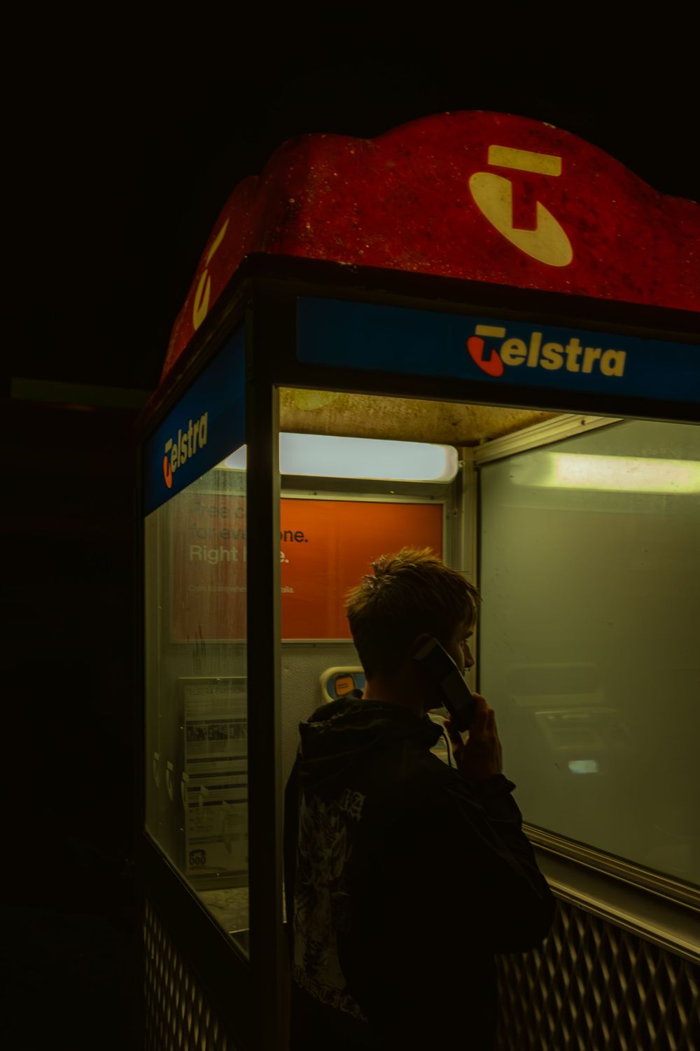 Illuminated Telstra phone booth glowing in the dark at night.