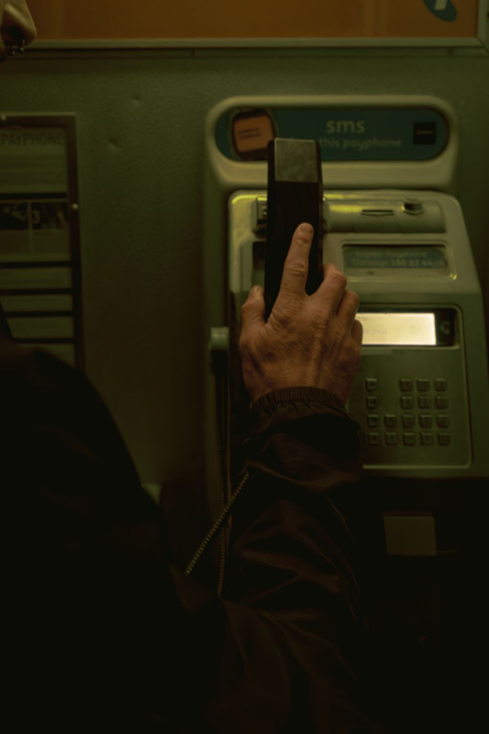 Close-up of hands interacting with a public payphone interface.
