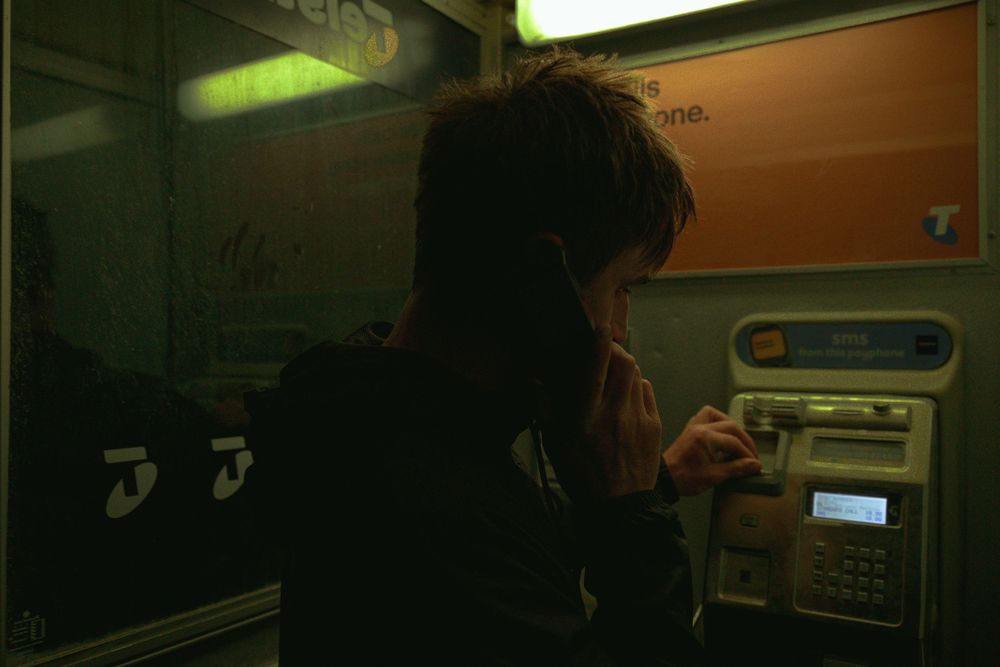 Person using a public phone booth under greenish fluorescent lighting.