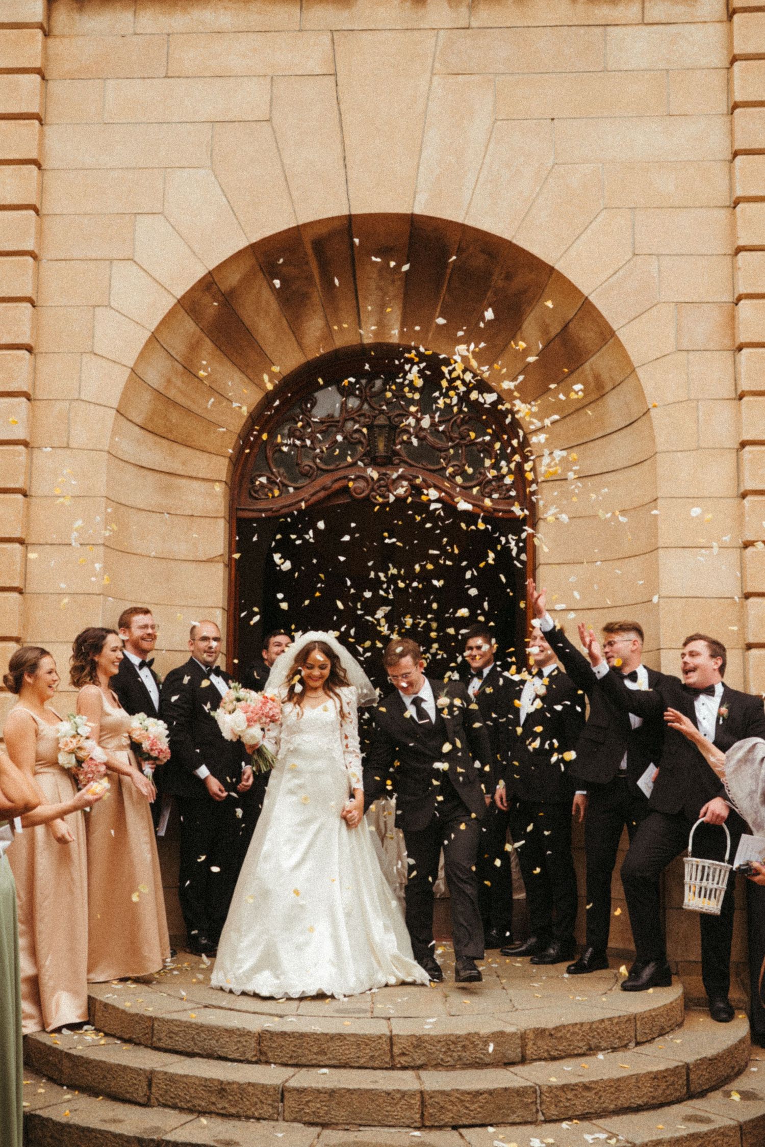 Wedding celebration with confetti being thrown outside stone archways.