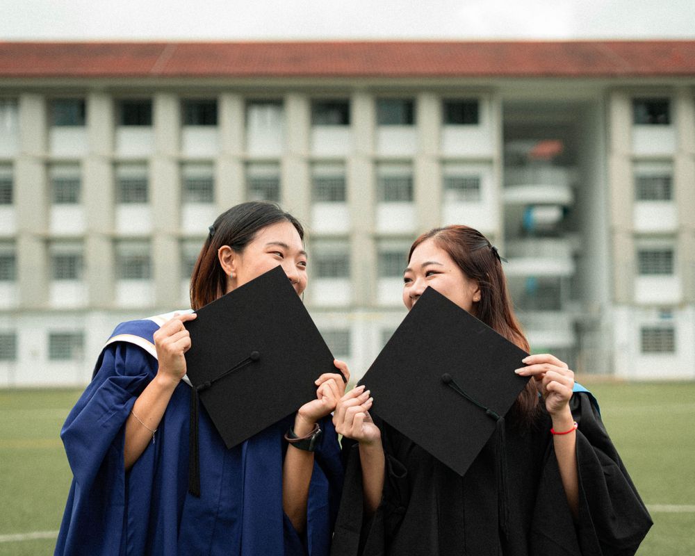 Two graduates playfully hide behind their mortarboards on graduation day.