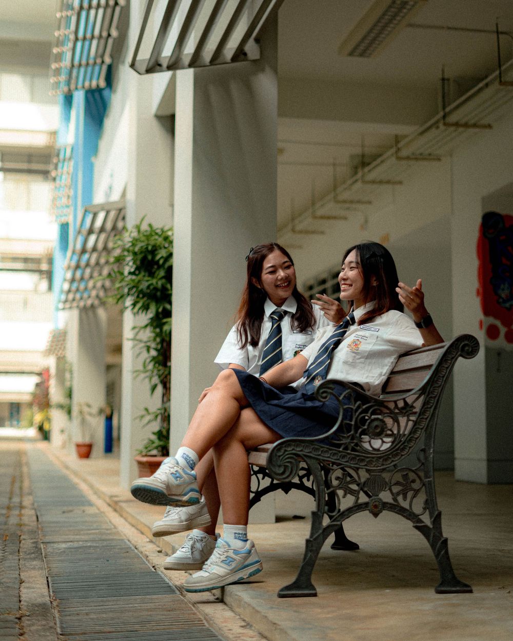 Students in school uniforms sharing a laugh while sitting on a vintage bench outside.